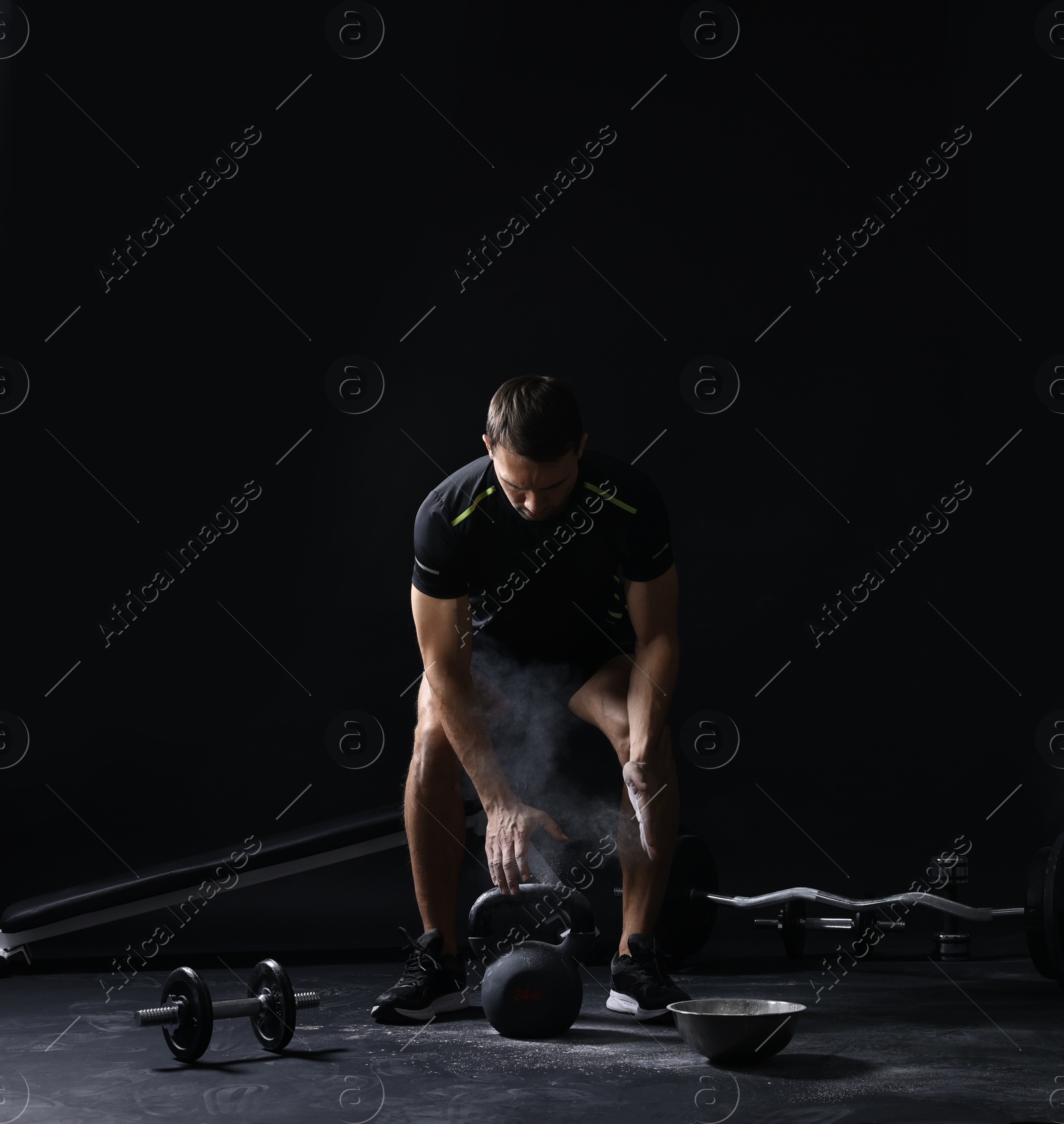 Photo of Man with talcum powder on hands training with kettlebell against black background