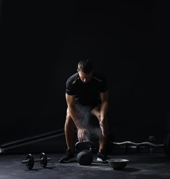 Photo of Man with talcum powder on hands training with kettlebell against black background