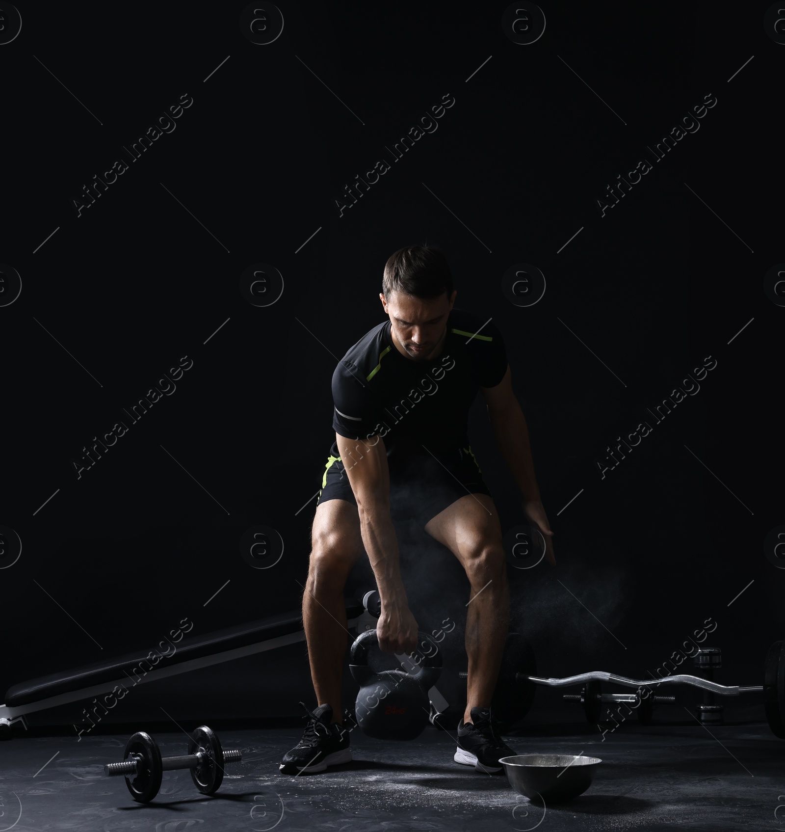 Photo of Man with talcum powder on hands training with kettlebell against black background