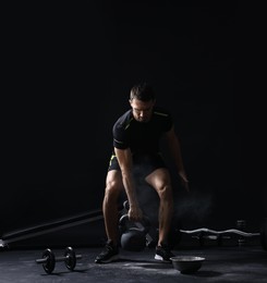 Photo of Man with talcum powder on hands training with kettlebell against black background