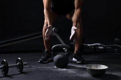 Photo of Man clapping hands with talcum powder before training with kettlebell on black background, closeup