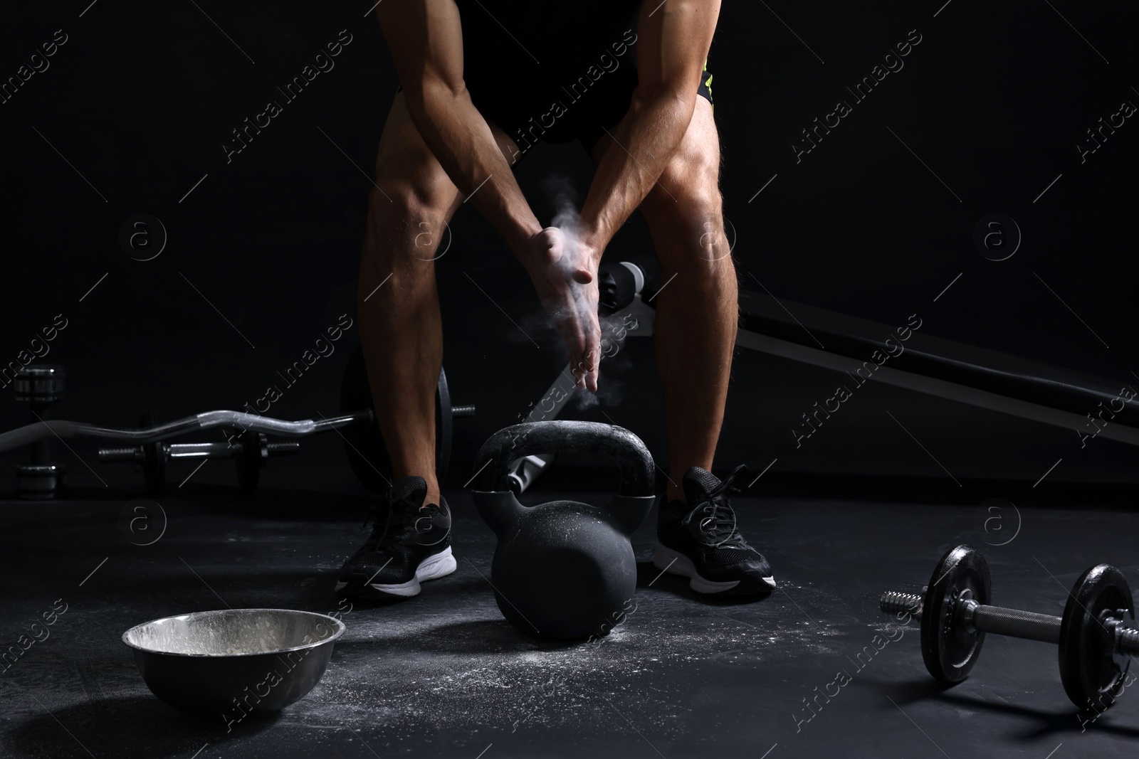 Photo of Man clapping hands with talcum powder before training with kettlebell on black background, closeup