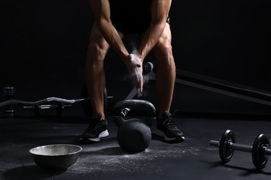 Photo of Man clapping hands with talcum powder before training with kettlebell on black background, closeup