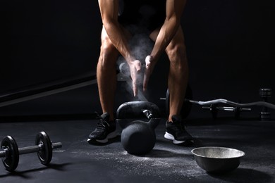 Photo of Man clapping hands with talcum powder before training with kettlebell on black background, closeup