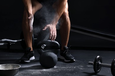 Photo of Man with talcum powder on hands training with kettlebell against black background, closeup