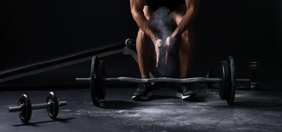 Photo of Man clapping hands with talcum powder before training with barbell on black background