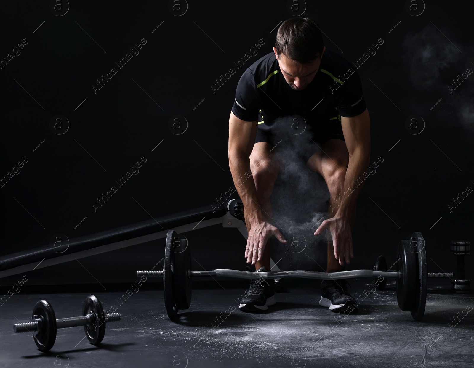 Photo of Man with talcum powder on hands training with barbell against black background