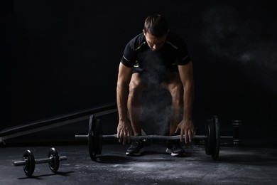 Man with talcum powder on hands training with barbell against black background