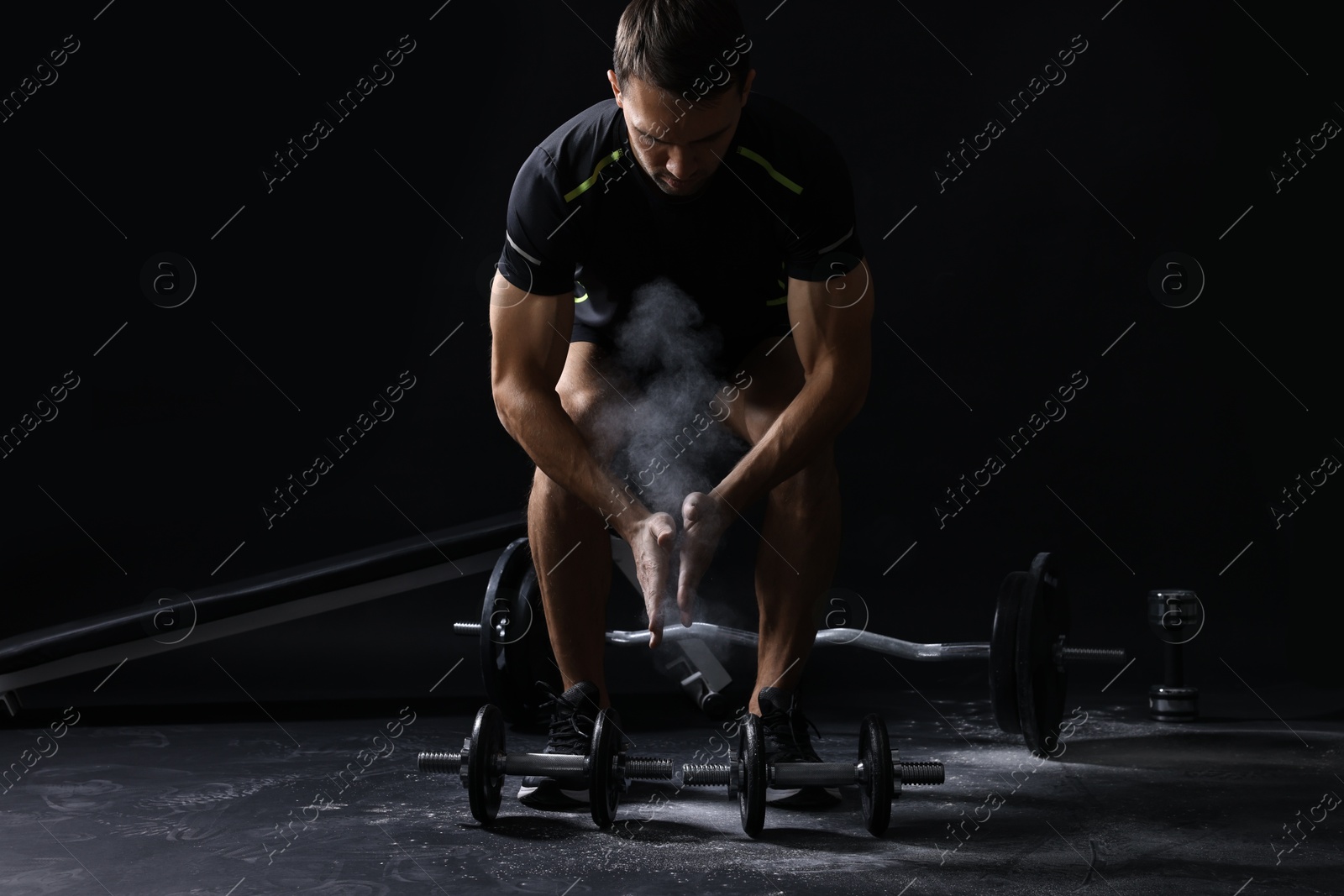 Photo of Man clapping hands with talcum powder before training with barbells on black background