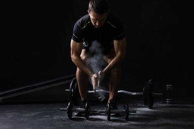 Photo of Man clapping hands with talcum powder before training with barbells on black background