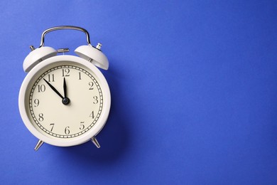 Photo of One white alarm clock on blue background, top view. Space for text