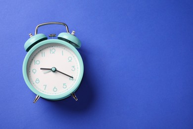 Photo of One turquoise alarm clock on blue background, top view. Space for text