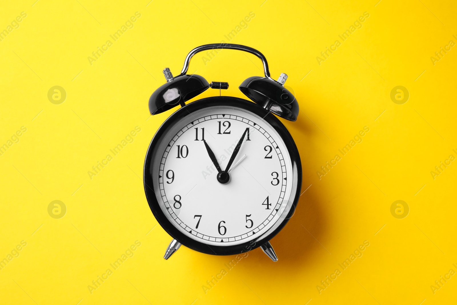 Photo of Black alarm clock on yellow background, top view