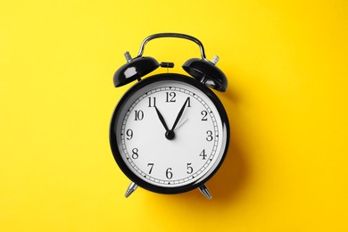 Photo of Black alarm clock on yellow background, top view