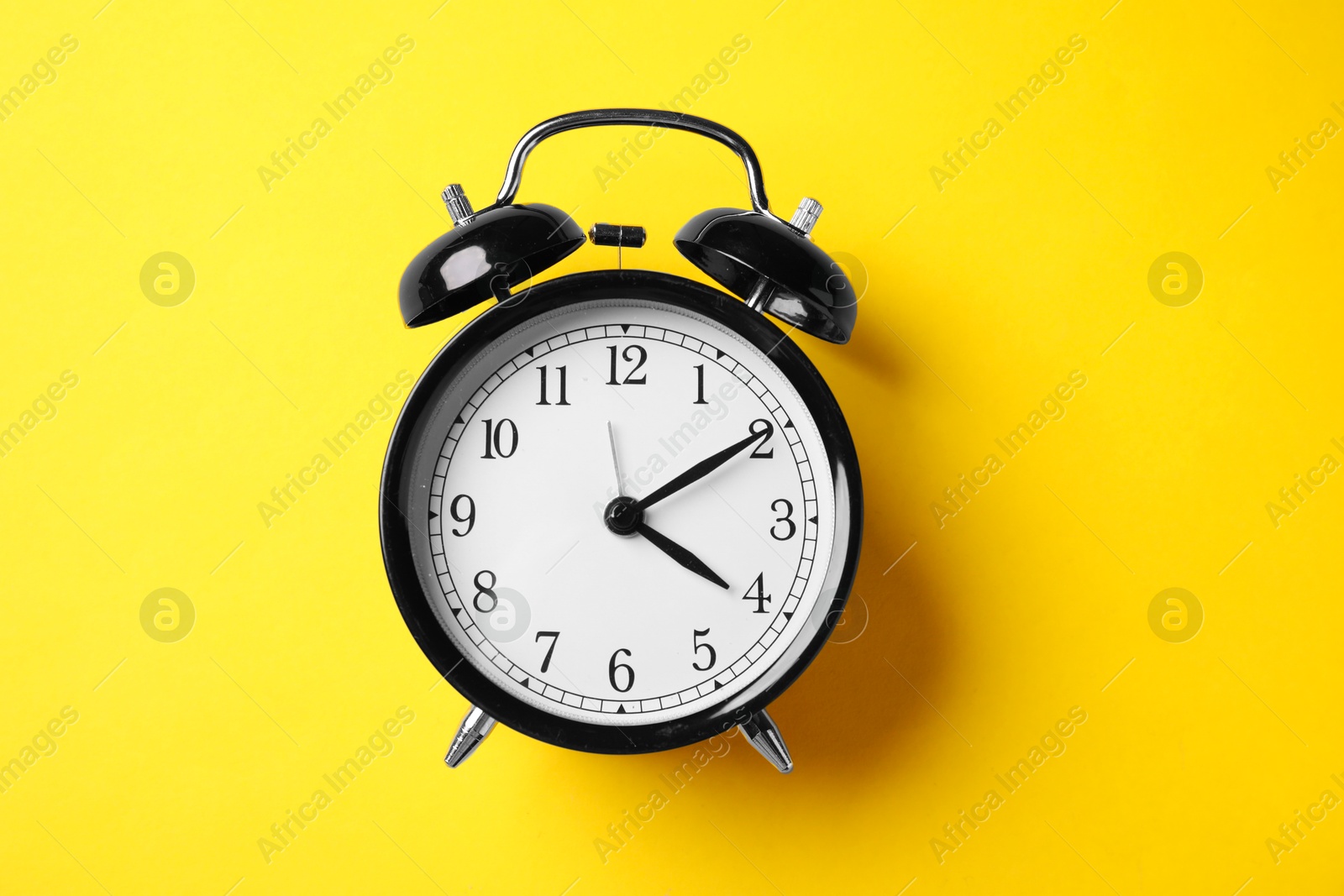 Photo of Black alarm clock on yellow background, top view