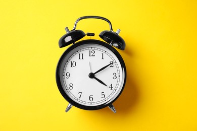 Photo of Black alarm clock on yellow background, top view