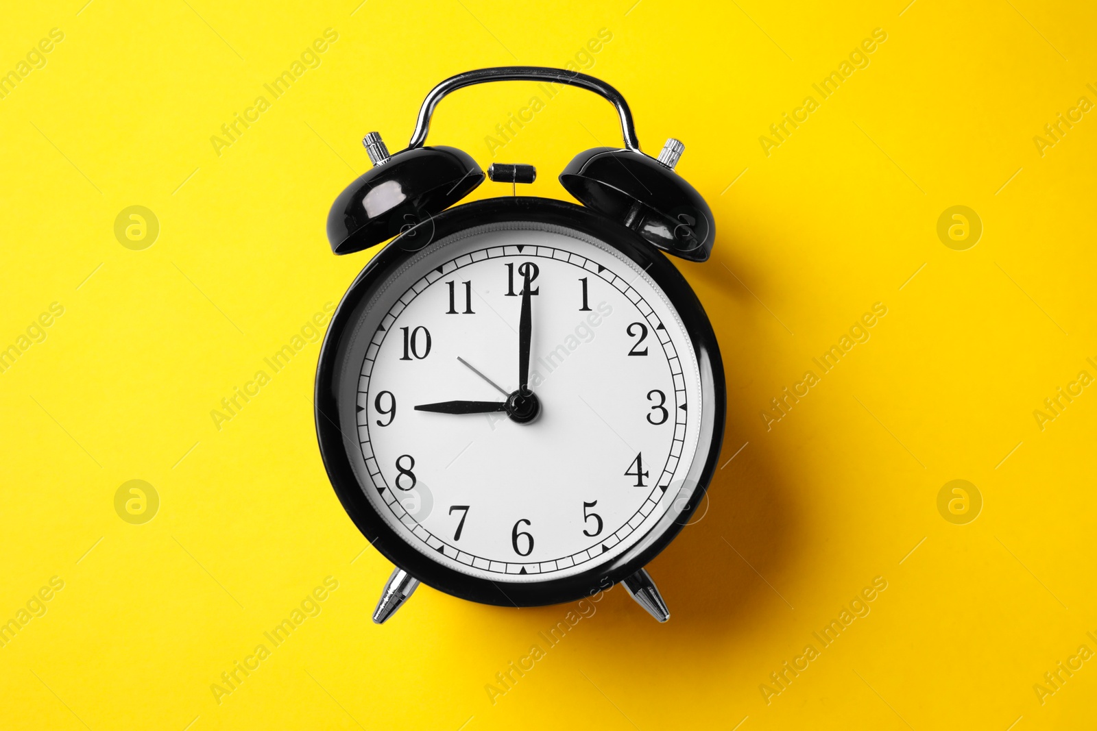 Photo of Black alarm clock on yellow background, top view