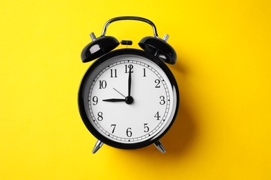 Photo of Black alarm clock on yellow background, top view