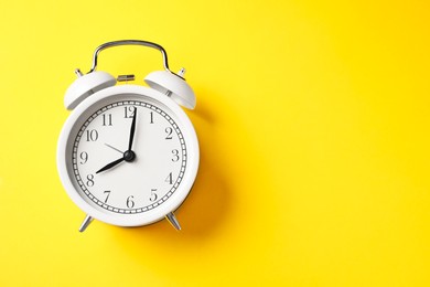 Photo of White alarm clock on yellow background, top view. Space for text