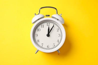 Photo of White alarm clock on yellow background, top view