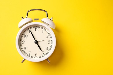 Photo of White alarm clock on yellow background, top view. Space for text