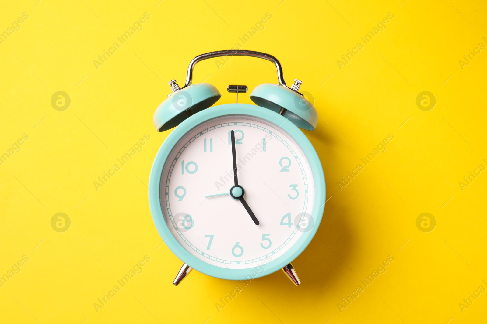Photo of Turquoise alarm clock on yellow background, top view