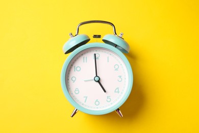 Photo of Turquoise alarm clock on yellow background, top view