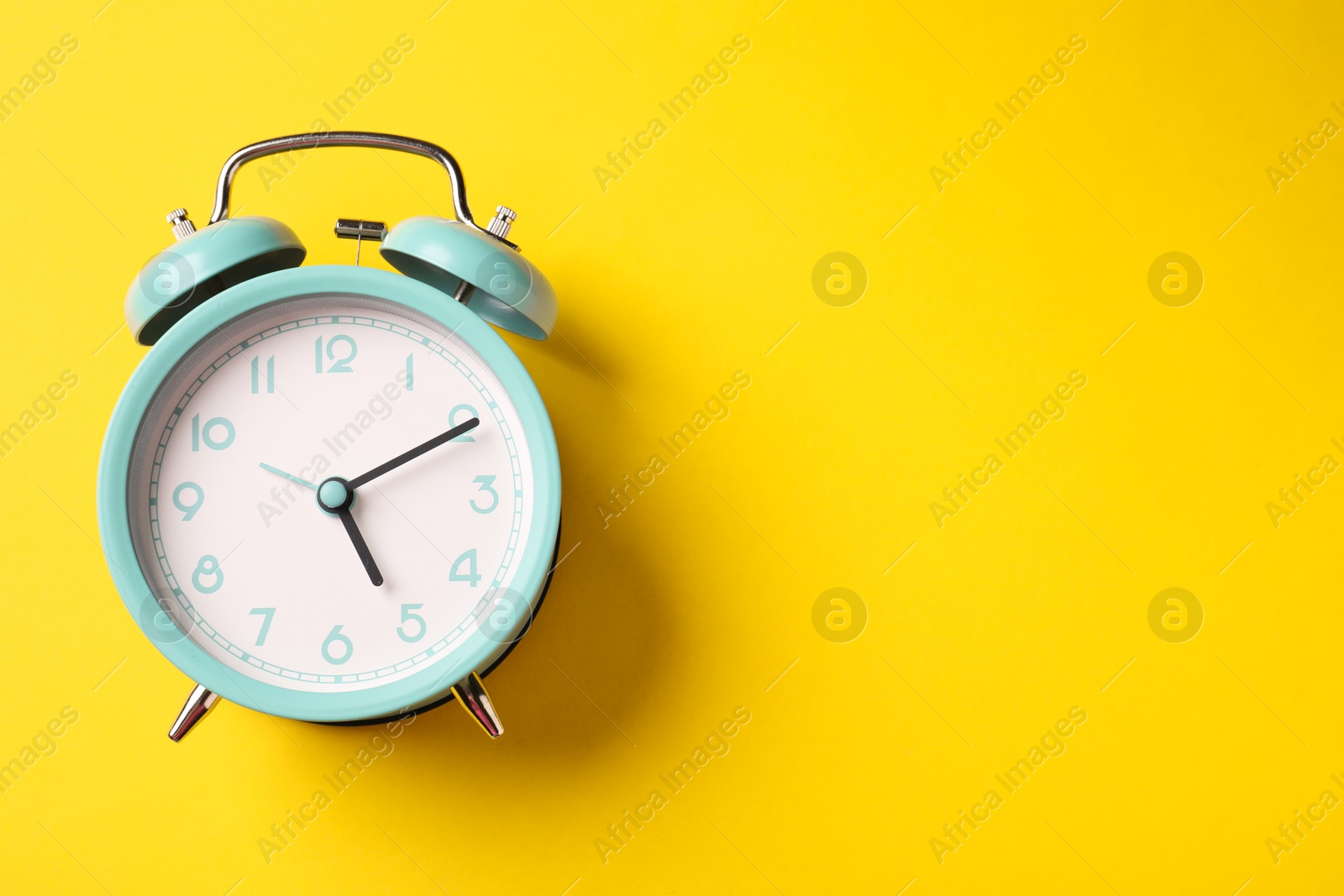 Photo of Turquoise alarm clock on yellow background, top view. Space for text