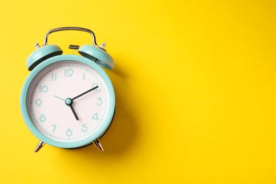Photo of Turquoise alarm clock on yellow background, top view. Space for text