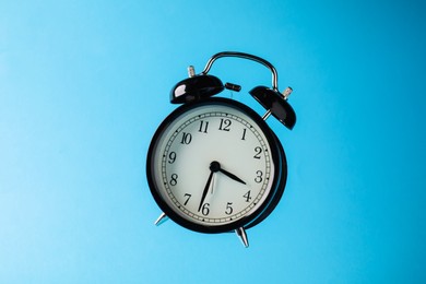 Photo of Black alarm clock in air on light blue background