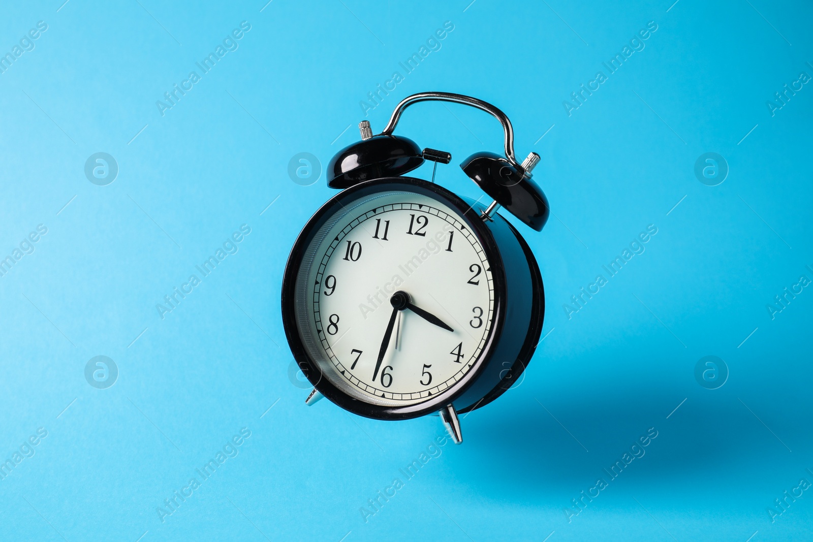 Photo of Black alarm clock in air on light blue background