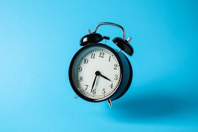 Photo of Black alarm clock in air on light blue background