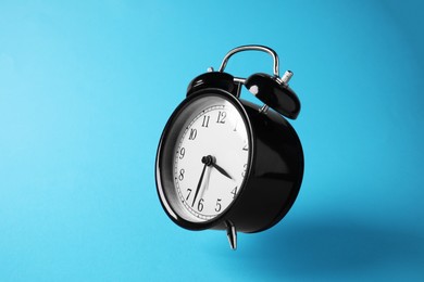Photo of Black alarm clock in air on light blue background