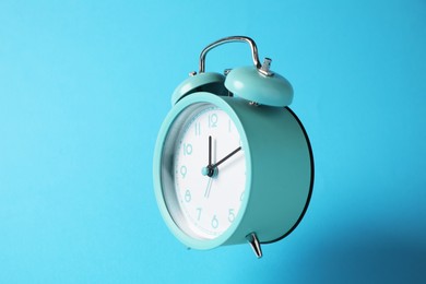 Photo of Turquoise alarm clock in air on light blue background