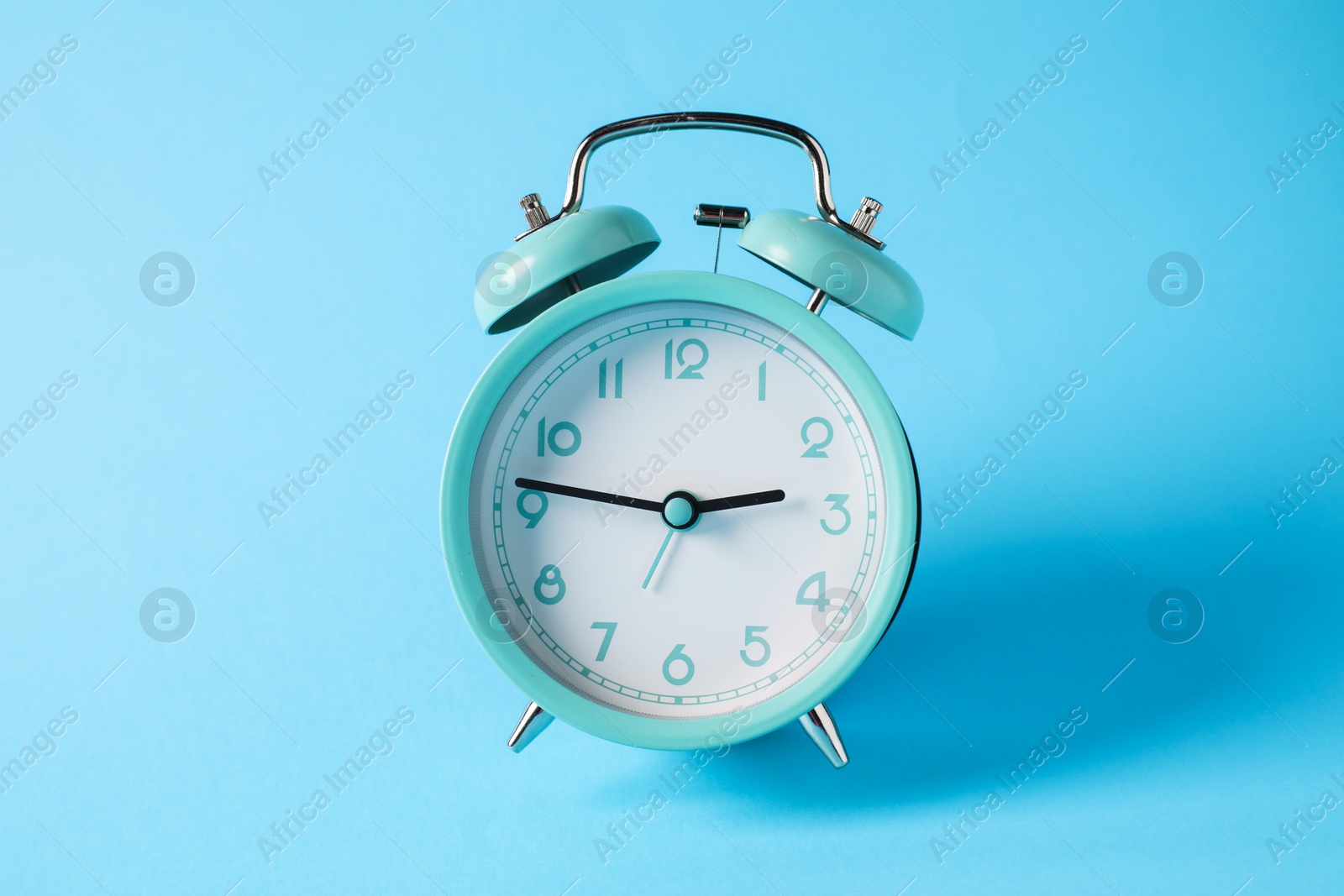 Photo of Turquoise alarm clock in air on light blue background