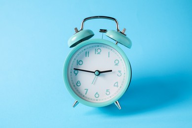 Photo of Turquoise alarm clock in air on light blue background