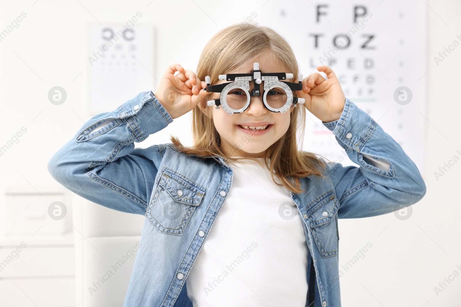 Photo of Vision testing. Little girl with trial frame at ophthalmologist office