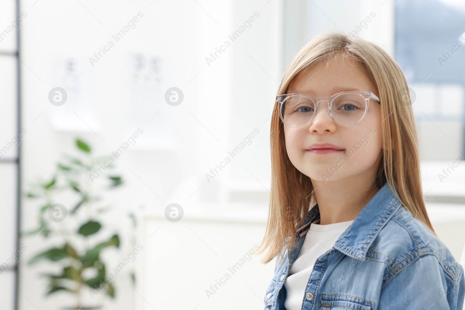 Photo of Little girl trying glasses at ophthalmologist office, space for text