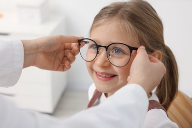 Vision testing. Ophthalmologist giving glasses to little girl in clinic, closeup