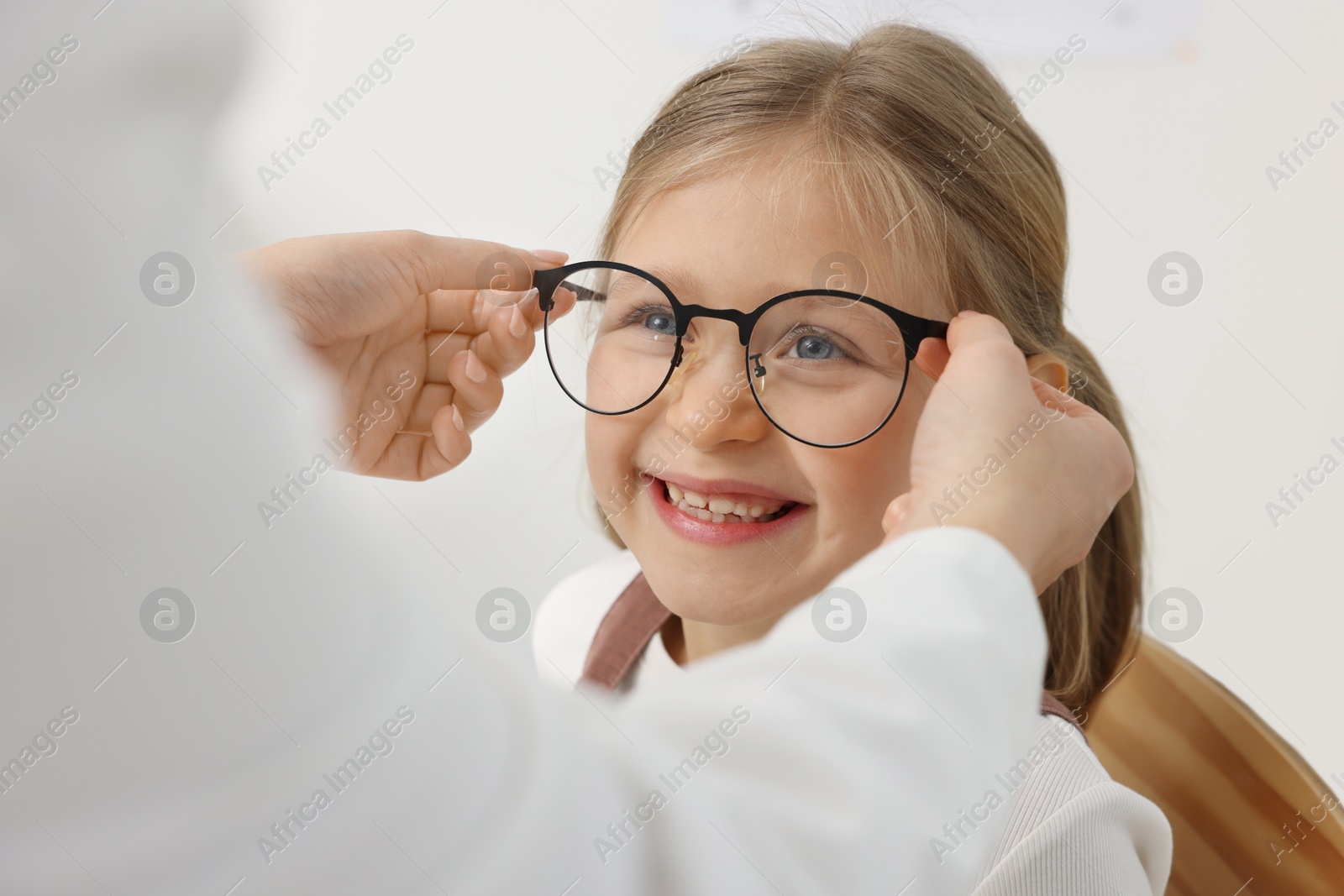 Photo of Vision testing. Ophthalmologist giving glasses to little girl in clinic, closeup