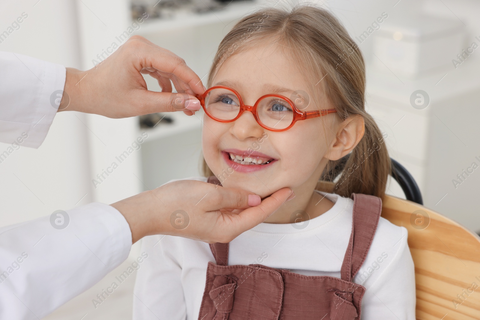 Photo of Vision testing. Ophthalmologist giving glasses to little girl in clinic, closeup