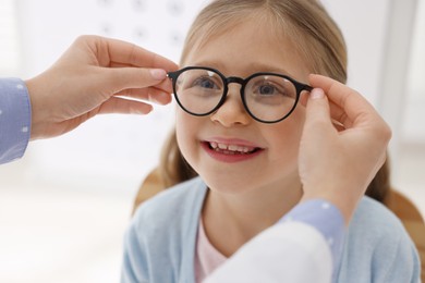 Photo of Vision testing. Ophthalmologist giving glasses to little girl indoors, closeup