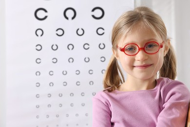 Photo of Little girl trying glasses against vision test chart