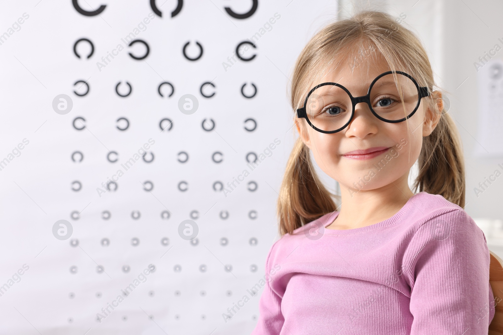 Photo of Little girl trying glasses against vision test chart