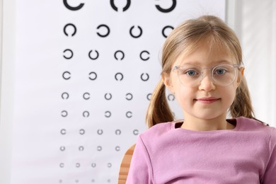 Photo of Little girl trying glasses against vision test chart