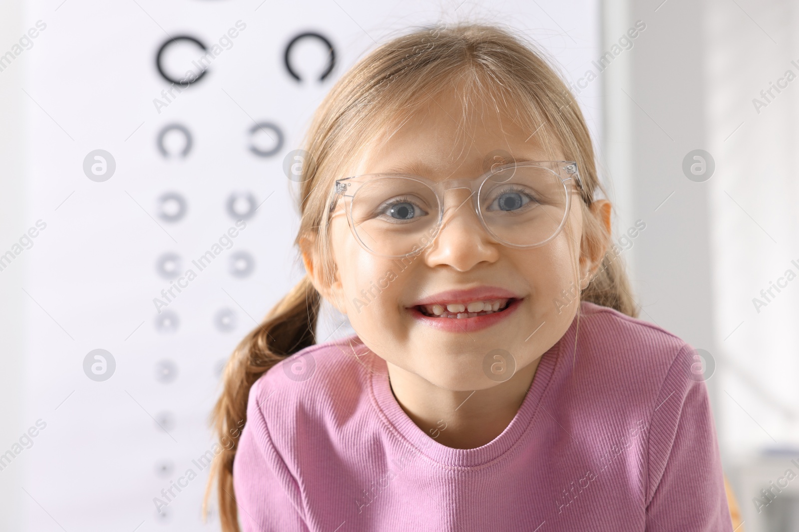 Photo of Little girl trying glasses against vision test chart