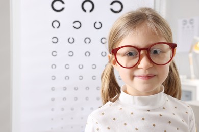 Photo of Little girl trying glasses against vision test chart