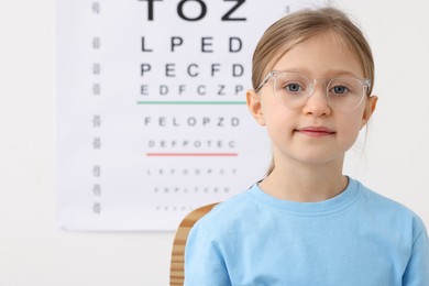 Photo of Little girl trying glasses against vision test chart