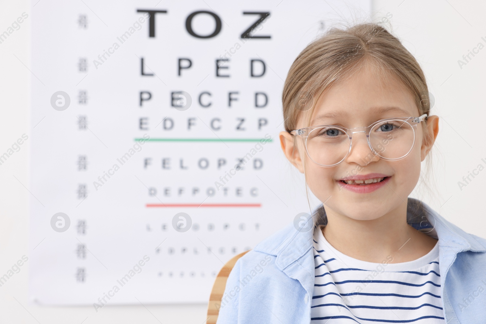 Photo of Little girl trying glasses against vision test chart