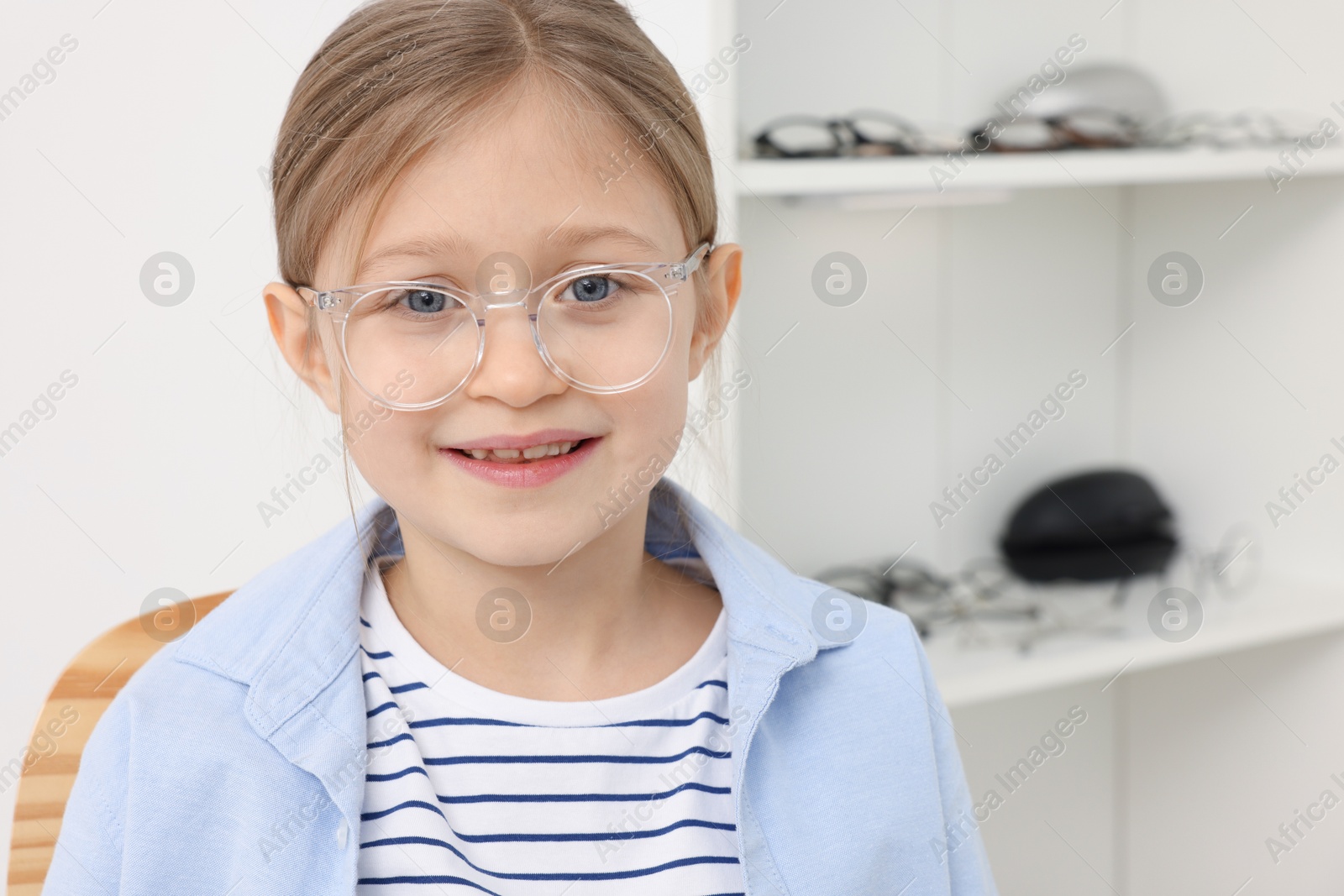 Photo of Little girl trying glasses at ophthalmologist office, space for text